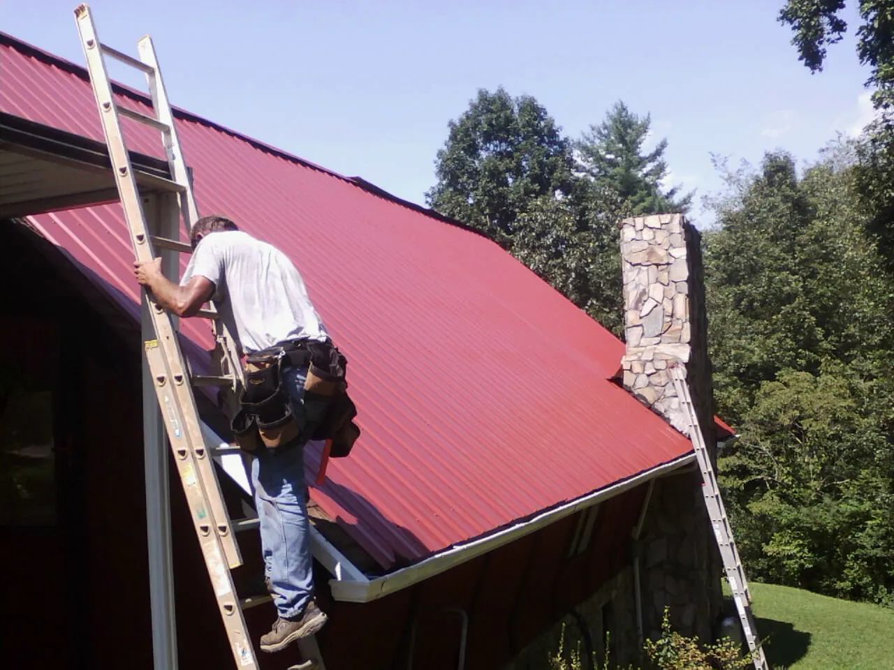 Roofer on a ladder beside a red metal roof and stone chimney in Chillicothe