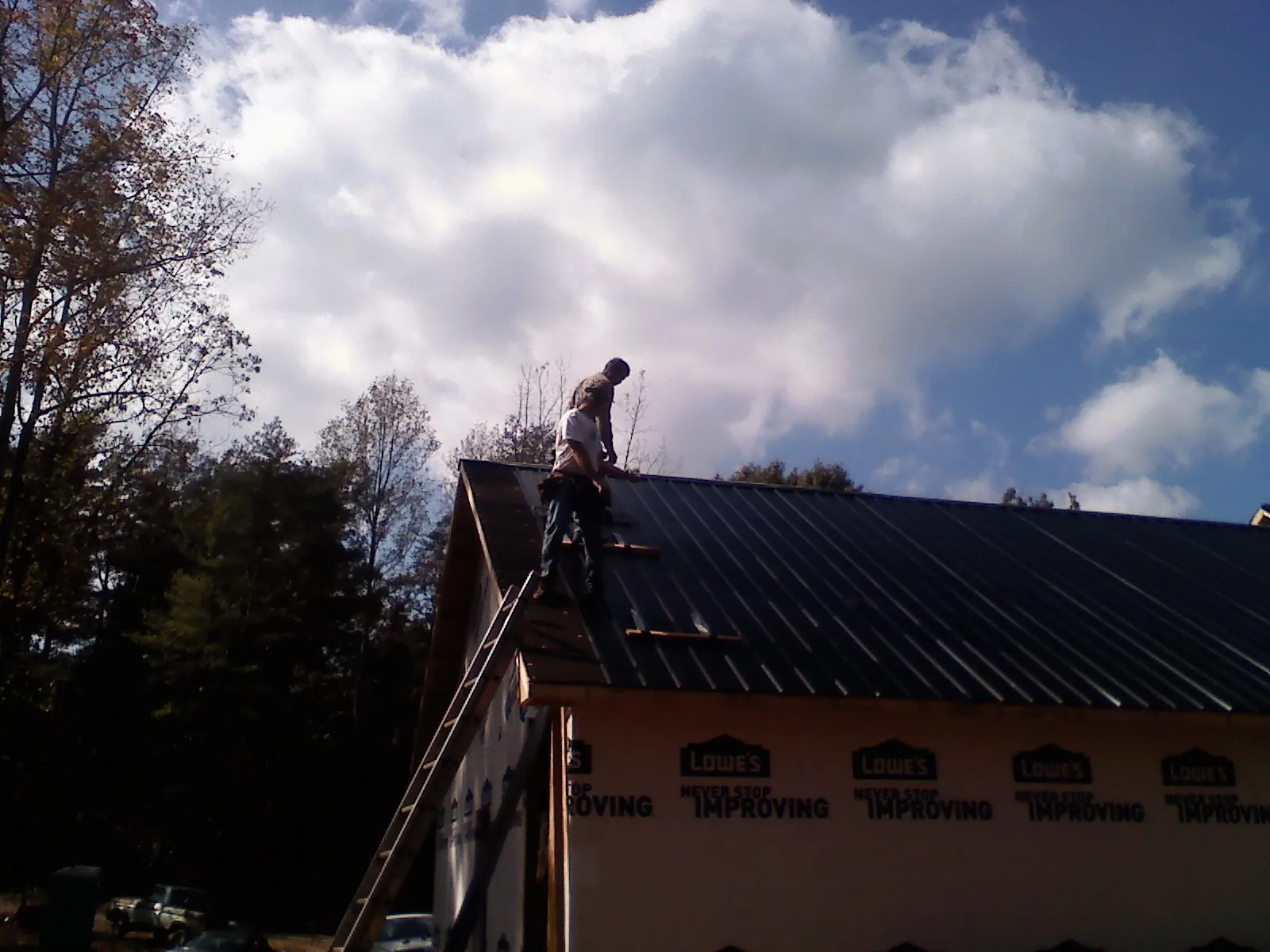 Roofer fastening dark metal panels high against a cloudy sky, from a Roof Inspection job in Chillicothe